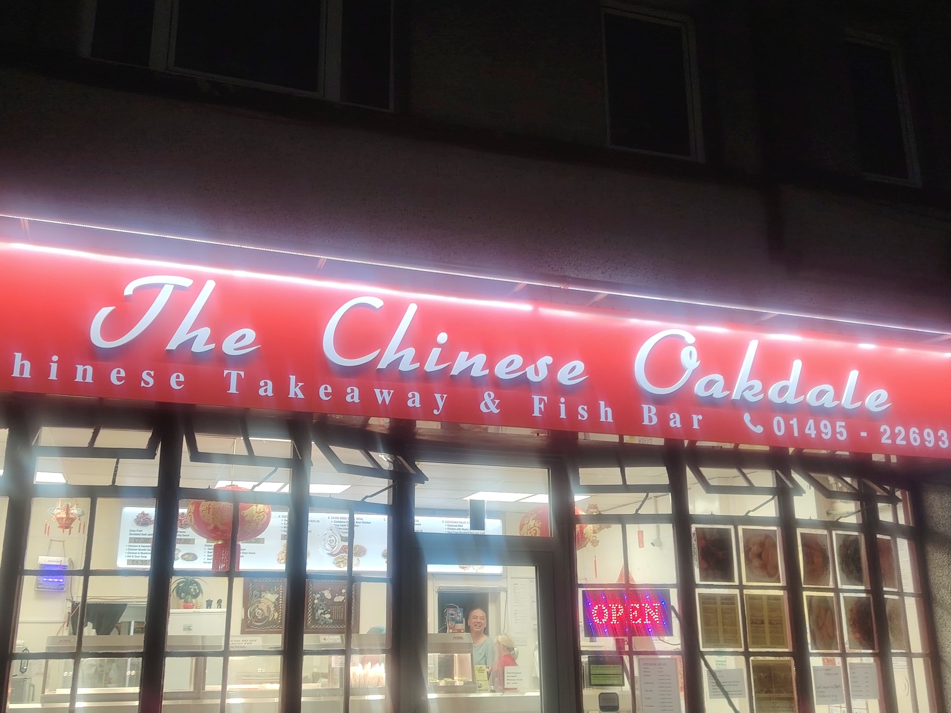 The Chinese Oakdale shopfront lit up at night — red signage in flowing script above the window