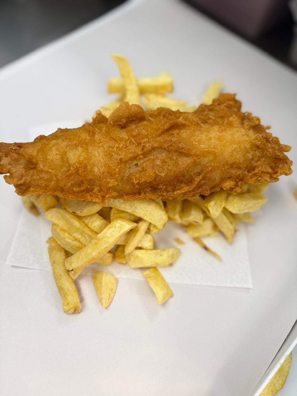Golden battered fish resting on hand-cut chips